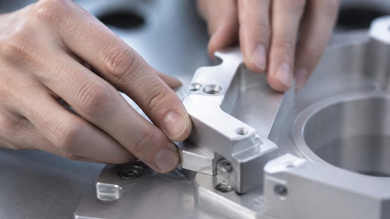 Two hands fitting a machined aluminium part into an assembly on a workbench